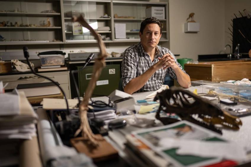 Faculty researcher Patrick O'Connor poses at his desk surrounded by paperwork and dinosaur bones