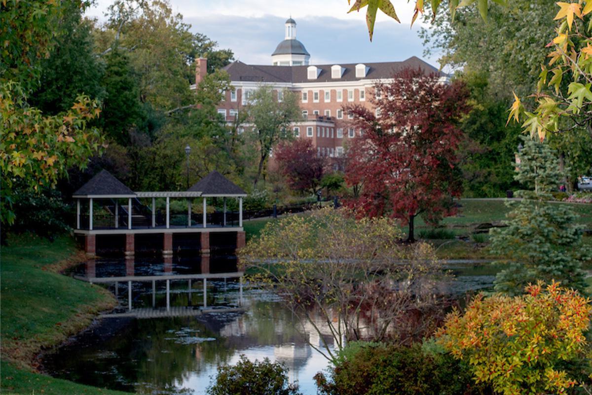 newbb电子平台埃默里蒂公园, featuring fall foliage surrounding a small pond on campus, with a brick building in the background